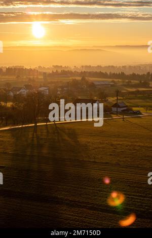 sunrise with sun shining into the camera above Dürrenmettstetten village in germany swabia with hazy landscape Stock Photo