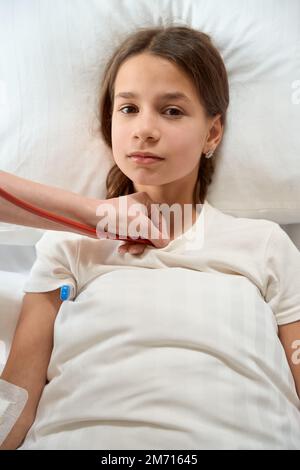 Sad girl lies on bed with thermometer under her arm Stock Photo