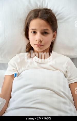 Pretty girl lies on bed with thermometer under her arm Stock Photo