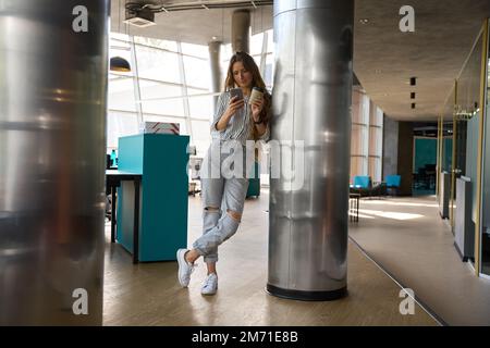Smiling lady holding coffee and reading messages in the office Stock Photo