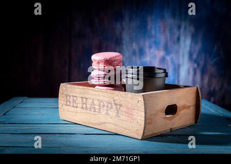 Macaroons and coffee in a wooden tray. Multicolored macaroons and coffee in a wooden box. Colored background. Stock Photo