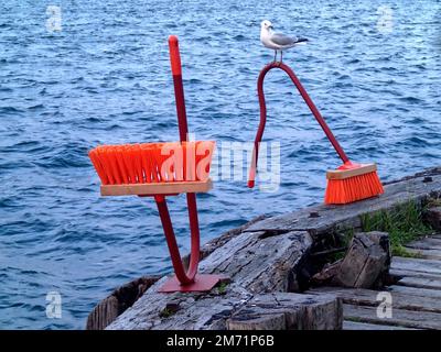 Orange broom sculptures on a Wellington harbour fishing wharf, with a common red-billed gull (Chroicocephalus novaehollandiae scopulinus), Stock Photo