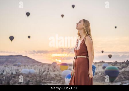 Tourist woman looking at hot air balloons in Cappadocia, Turkey. Happy Travel in Turkey concept. Woman on a mountain top enjoying wonderful view Stock Photo