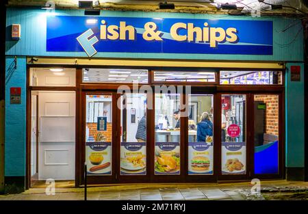 Fish and Chip shop at night with 2 people outside waiting for their ...