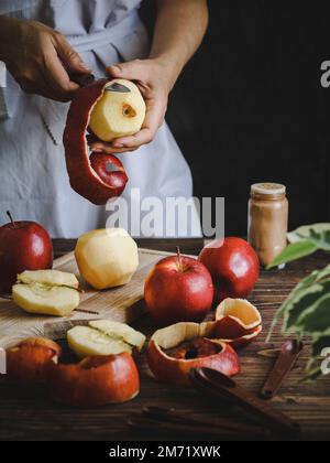 Woman peeling red apples on a cutting board over a rustic dark wooden table Stock Photo