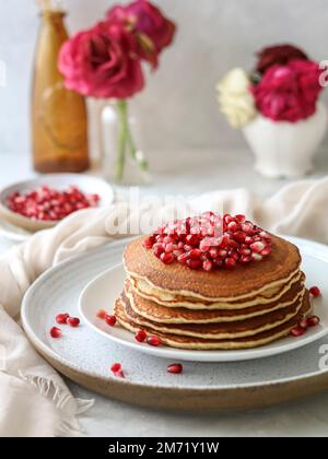 Stack of pancakes decorated with pomegranate and red flowers on a light background Stock Photo