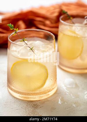Glass of water with ice cubes decorated with a lemon slice and thyme Stock Photo