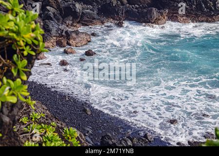Small isolated beach with black stones and blue waves on Maui island, Hawaii Stock Photo