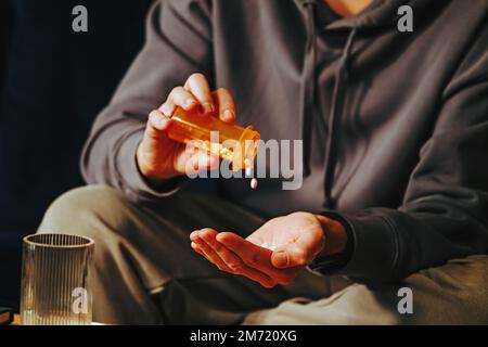 Close-up shot of man pouring tablets from orange plastic bottle into his hand. Medication, addiction, pain concept Stock Photo