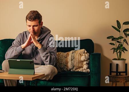 Man looking on the tablet while sitting on his couch. Online therapy, mental health Stock Photo
