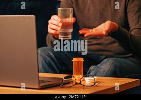 Unrecognizable man taking medicine while working at the laptop. Pain relief, headache Stock Photo