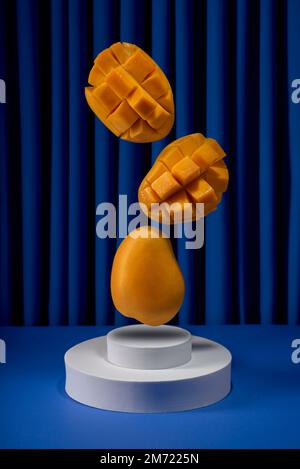 fresh sliced mango for cocktail, flying fruit minimal style on blue background, no people Stock Photo