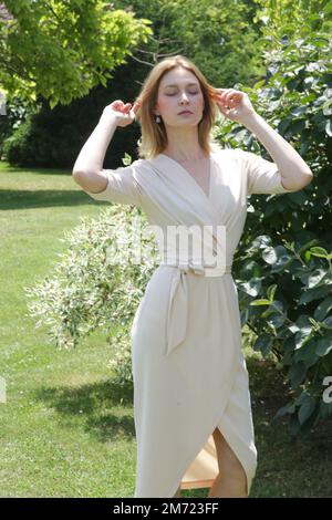Portrait of attractive young woman wearing elegant cream midi wrap dress in the restaurant garden