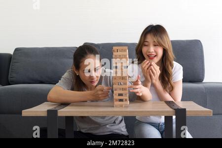 Two asian woman enjoy playing  wooden blocks game in the living room. Players take turns removing one block at a time from a tower constructed of 54 b Stock Photo