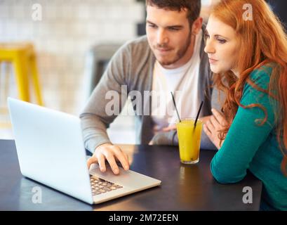 Enjoying any time spent together. a young couple using a laptop while having a drink at a cafe. Stock Photo