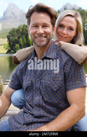 Carefree couple. Portrait of a loving mature couple sitting beside a lake in the countryside. Stock Photo