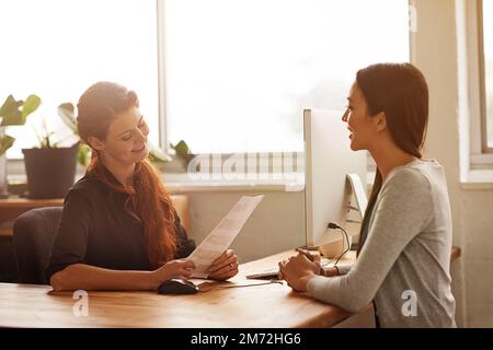 Tell me more about yourself...two young businesswomen having a discussion at a desk. Stock Photo