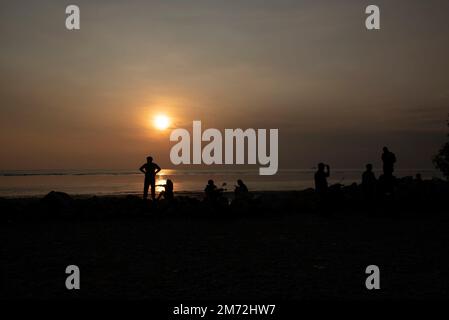 Scene of a few unknown silhouette people relaxing on the seaside in the dark viewing the evening setting sun Stock Photo