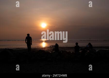 Scene of a few unknown silhouette people relaxing on the seaside in the dark viewing the evening setting sun Stock Photo