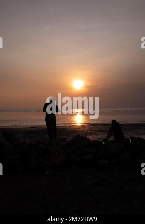 Scene of a few unknown silhouette people relaxing on the seaside in the dark viewing the evening setting sun Stock Photo