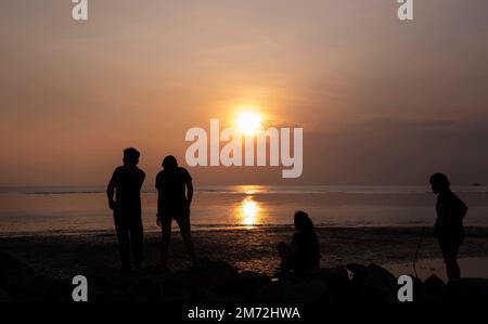 Scene of a few unknown silhouette people relaxing on the seaside in the dark viewing the evening setting sun Stock Photo