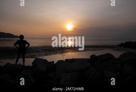 Scene of a few unknown silhouette people relaxing on the seaside in the dark viewing the evening setting sun Stock Photo