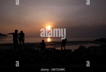 Scene of a few unknown silhouette people relaxing on the seaside in the dark viewing the evening setting sun Stock Photo