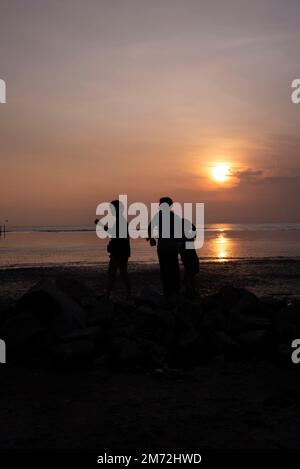 Scene of a few unknown silhouette people relaxing on the seaside in the dark viewing the evening setting sun Stock Photo