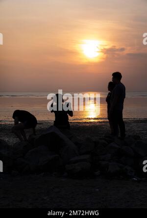 Scene of a few unknown silhouette people relaxing on the seaside in the dark viewing the evening setting sun Stock Photo