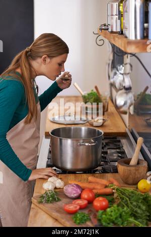 Mmm, quite tasty. a young woman tasting the food she is preparing in the kitchen. Stock Photo