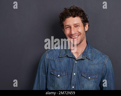 He tries not to be too serious. Studio portrait of a handsome man standing against a gray background. Stock Photo