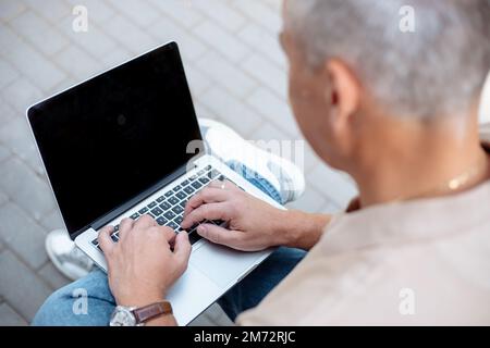 Unrecognizable gray haired businessman using laptop, black screen with place for advertisement text outdoors. IT job ad Stock Photo