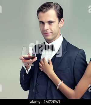 The all-too-eligible bachelor. womans arm touching a young man with a glass of wine wearing a vintage suit. Stock Photo