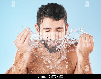 Man, splash and face for beauty in studio for wellness, health or self care cleaning by blue background. Model, bathroom and water drops with hands Stock Photo