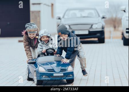 Three happy children playing with big old toy car in countryside, outdoors. Stock Photo