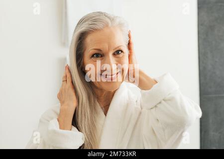 Portrait of a senior woman adjusting her grey hair while looking at the bathroom mirror Stock Photo