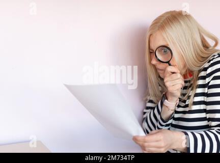 Funny mature woman  standing isolated over light background, reading document with magnifying glass Stock Photo
