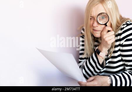 Funny mature woman  standing isolated over light background, reading document with magnifying glass Stock Photo