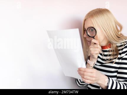 Funny mature woman  standing isolated over light background, reading document with magnifying glass Stock Photo