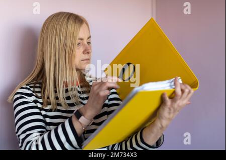 Middle-aged woman  standing isolated over light background and reading document with magnifying glass Stock Photo