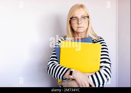 Mature  thoughtful business woman holding folders isolated on light background Stock Photo