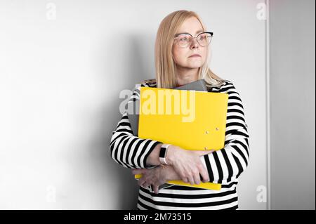 Mature  thoughtful business woman holding folders isolated on light background Stock Photo