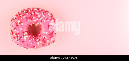 Pink donut with sprinkles on pink pastel background. One sweet pink donut. Top view. Copy space Stock Photo