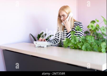Attractive middle-aged woman talks on phone at her workplace Stock Photo
