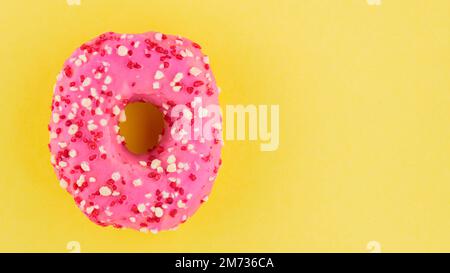 Strawberry donut with pink icing and sprinkles. Sweet pink donut on yellow background. Flat lay. Copy space Stock Photo