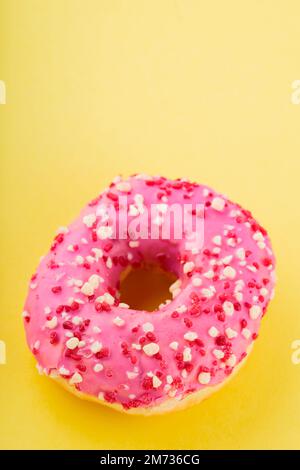 Strawberry donut with pink icing and sprinkles. Sweet pink donut on yellow background. Flat lay. Copy space Stock Photo