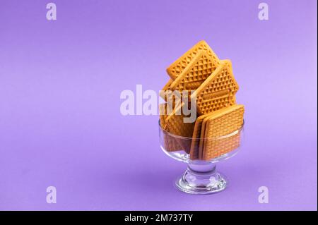 Stack of square biscuits in glass dish isolated on purple violet background Stock Photo