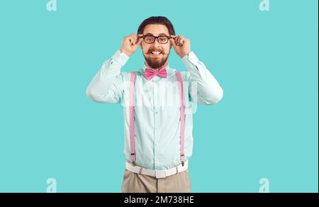 Young Caucasian man with funny beard and moustache smiling adjusts glasses, stands in studio Stock Photo