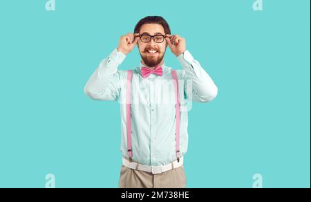 Young Caucasian man with funny beard and moustache smiling adjusts glasses, stands in studio Stock Photo