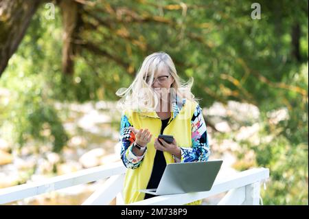 Attractive middle aged female using smartphone and laptop outdoor Stock Photo
